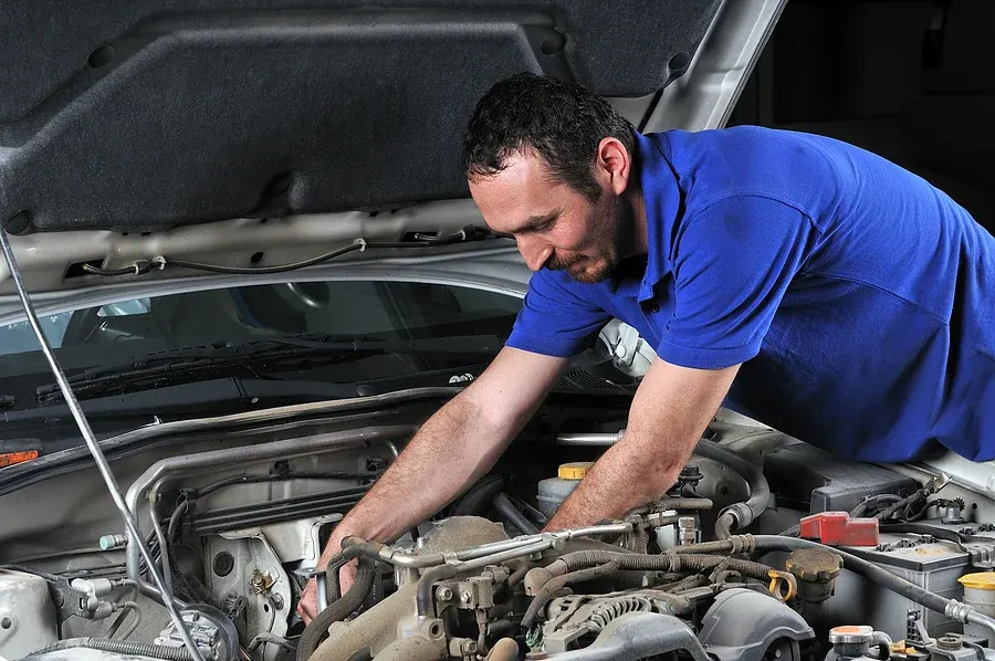 Automotive technician inspecting engine components beneath an open hood
